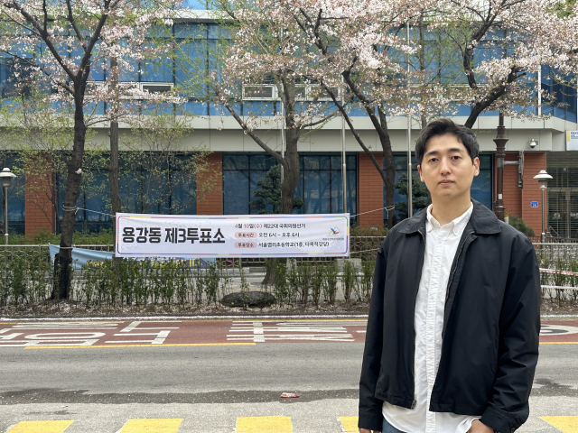 Lee Hyoun-jeek, 36, takes a photo in front of a polling station banner set up in front of Yeomri Elementary School in Mapo-gu, western Seoul, Wednesday. (Lee Jung-joo/The Korea Herald)