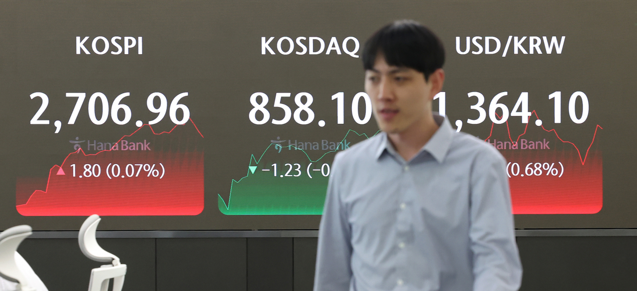 A currency trader passes by the screens showing the Kospi, Kosdaq and and the foreign exchange rate between US dollar and South Korean won at a KEB Hana Bank branch in Seoul, Thursday. (Yonhap)