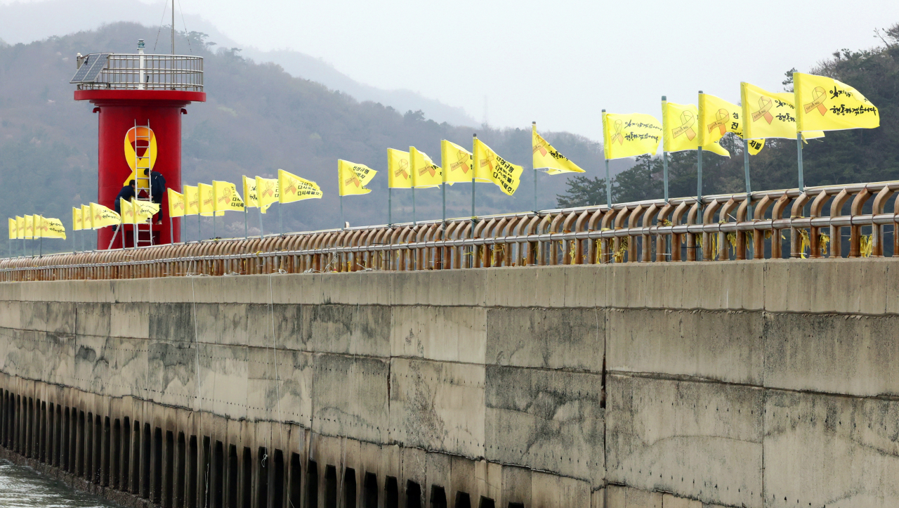 Workers paint a yellow ribbon on a lighthouse on the breakwater at Paengmok Port -- now known as Jindo Port -- at Jindo, South Jeolla Province on April 4. (Yonhap)