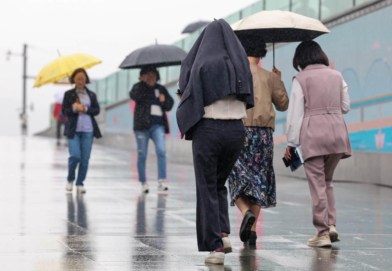 People walk near Gwanghwamun, Seoul, avoiding rain with jackets and umbrellas, Monday. (Yonhap)