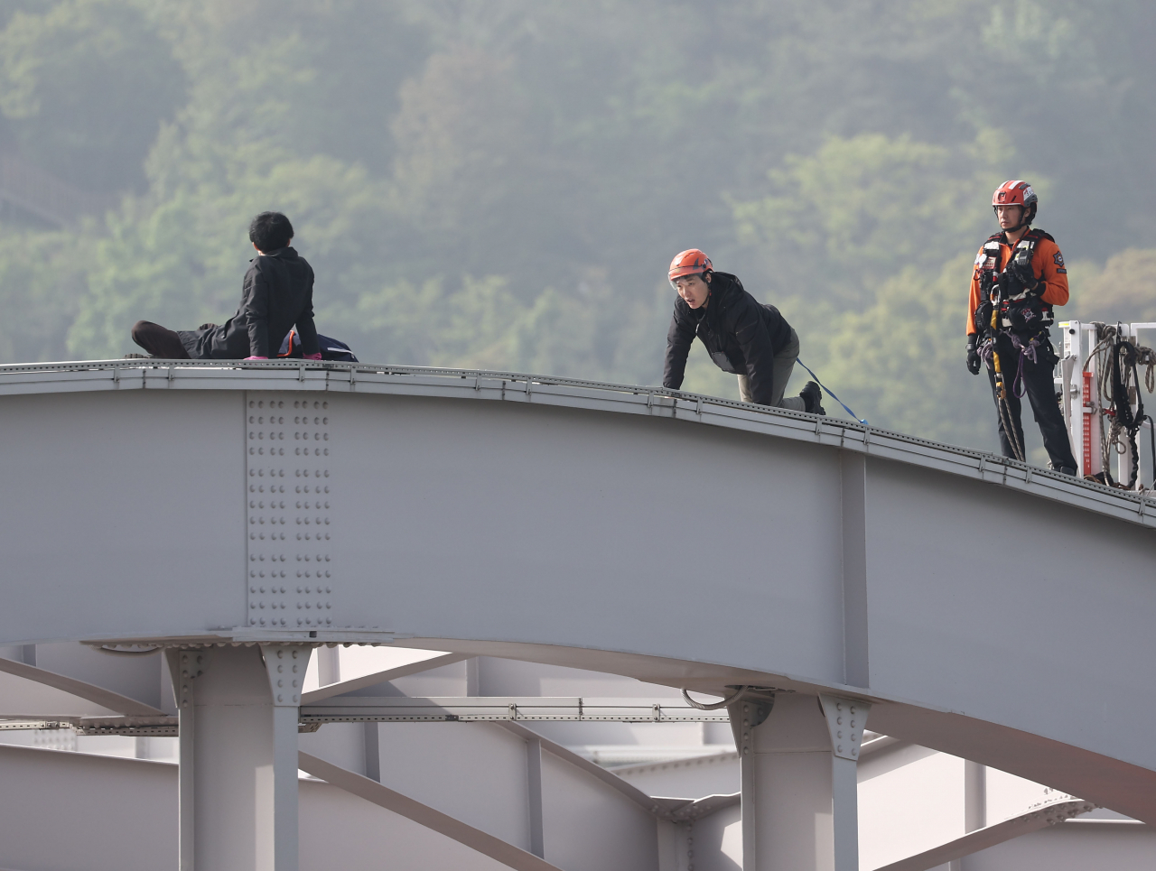 Seoul rescue workers talk to a man (left) who climbed on top of the Hangangdaegyo bridge and staged a five-hour protest, Wednesday. (Yonhap)
