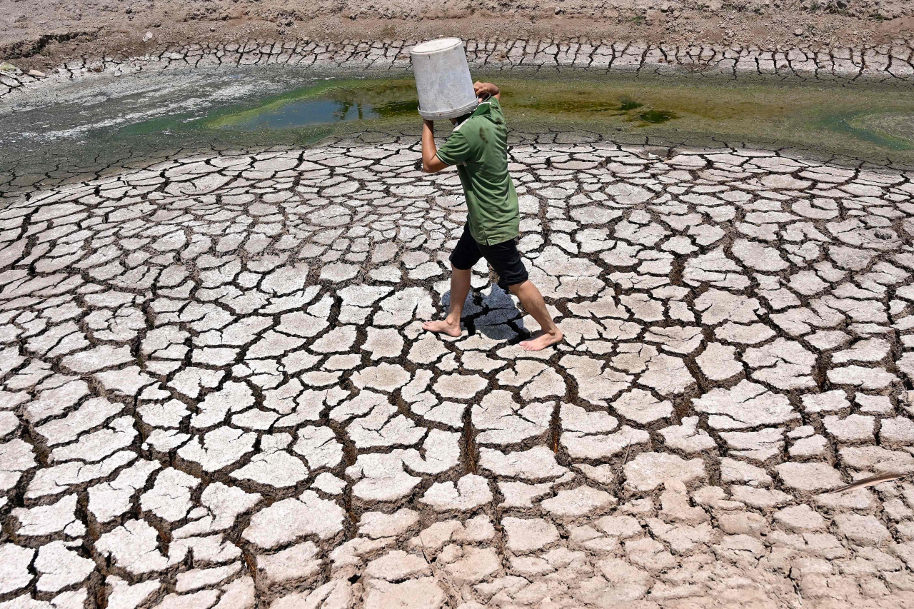 A man carries a plastic bucket across the cracked bed of a dried-up pond in Vietnam's southern Ben Tre province, March 19. (AFP-Yonhap)