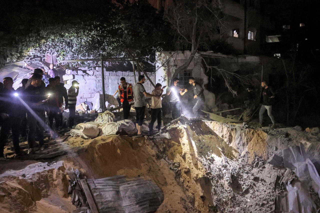 People search with flashlights by an impact crater at the site of a building that was hit by Israeli bombardment in Rafah in the southern Gaza Strip on Tuesday. (AFP-Yonhap)
