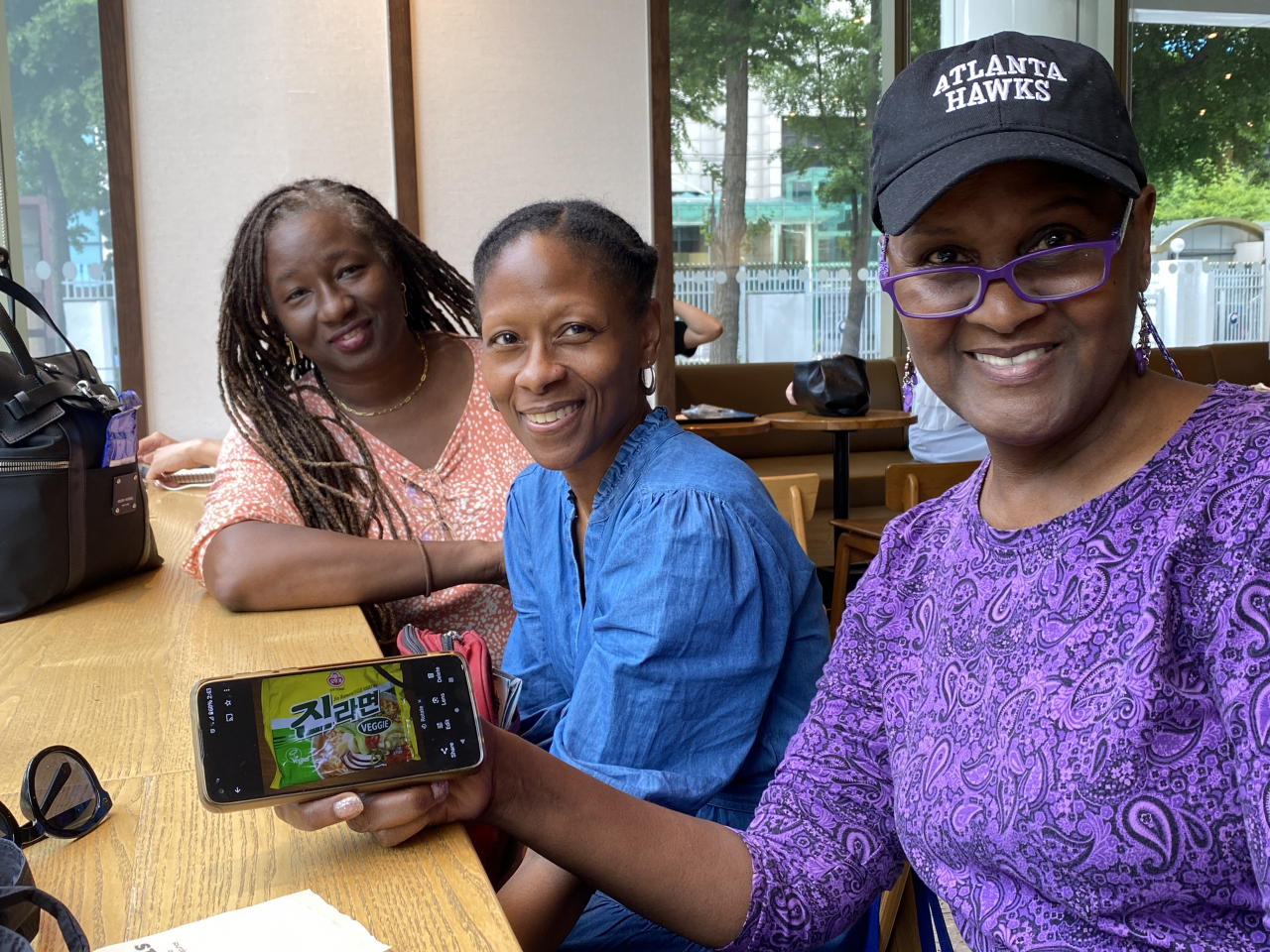 Cindy X. Jones (right), a 50-year-old African American from Georgia, the US, shows a picture of Ottogi’s vegan instant noodle on her smartphone while posing with her friends Shannon Ridley (center) and Le Tisha C. Campbell at a coffee shop in Seoul on Sunday. (Hwang Joo-young/The Korea Herald)