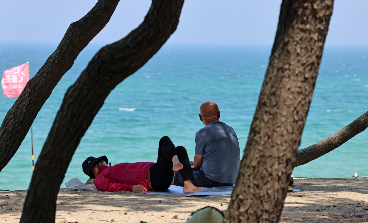 People rest under the shade near Songjeong Beach in Gangneung, Gangwon Province on Tuesday, after the first tropical night of the year was issued in the city on Monday night. (Yonhap)