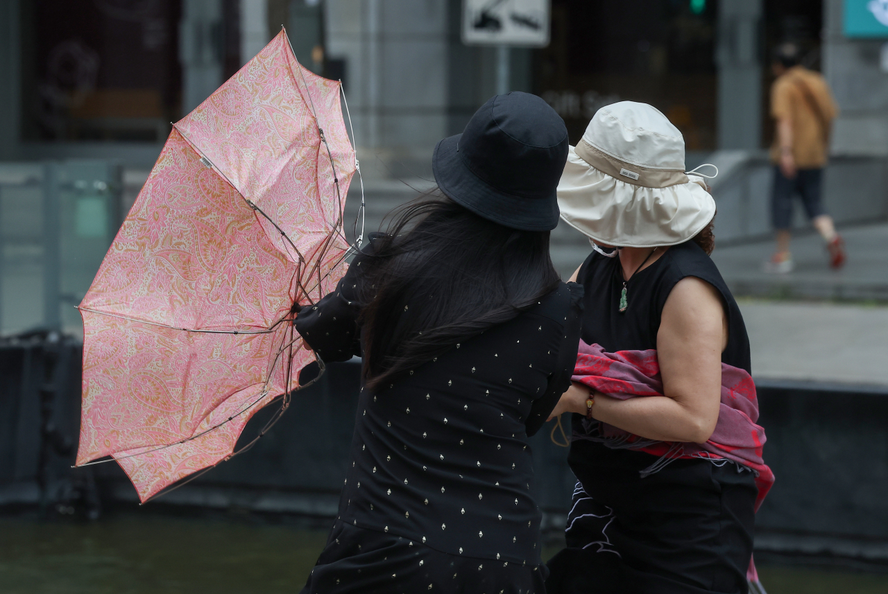 Tourists fix their umbrellas amid strong winds near Cheonggyecheon, in Jongno, central Seoul, Sunday. (Yonhap)