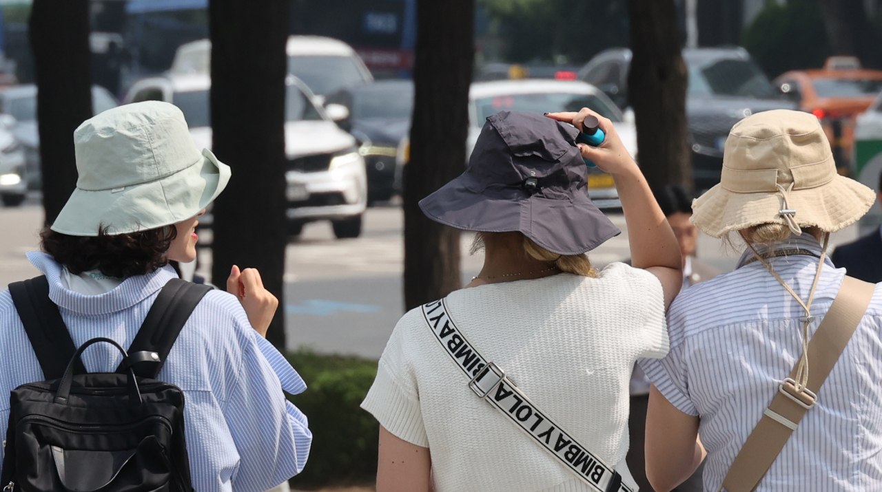 Foreigners stroll along a walkway while wearing hats in downtown Seoul on June 11. (Yonhap)