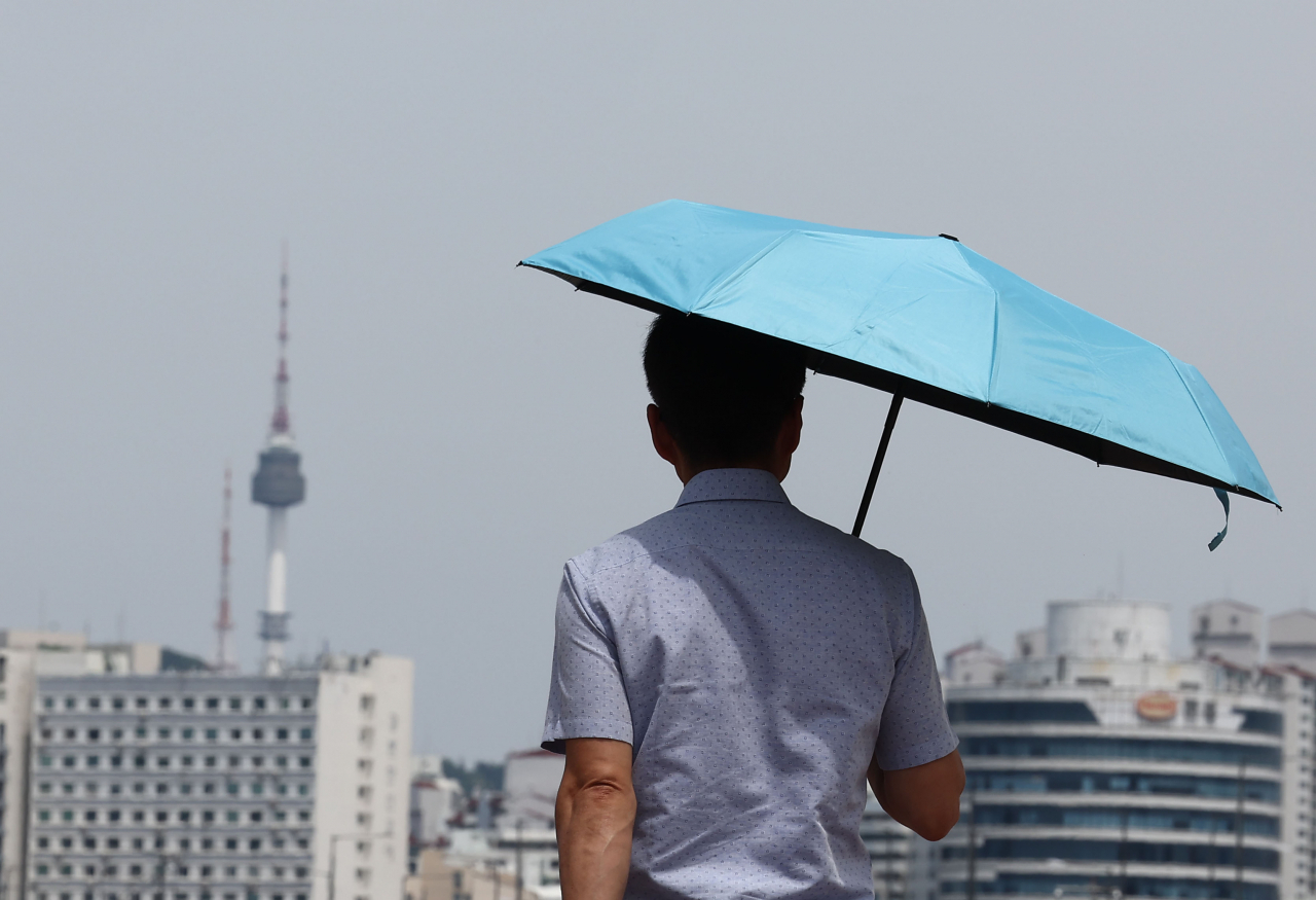 A pedestrian walks with a parasol on June 17 in Yeouido, western Seoul. (Yonhap)