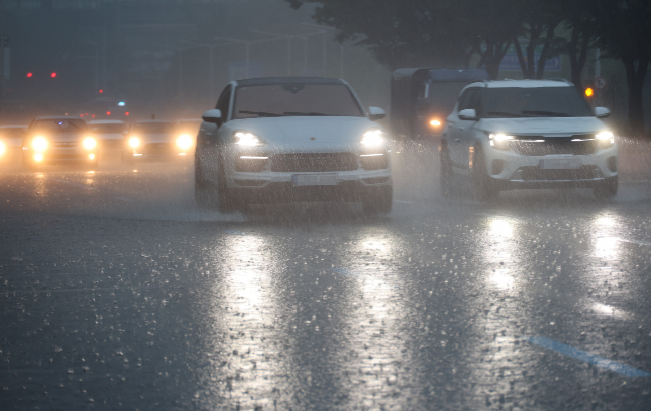 A car drives through the central city of Daejeon on Sunday, amid heavy rain, with its headlights on in the morning. (Yonhap)