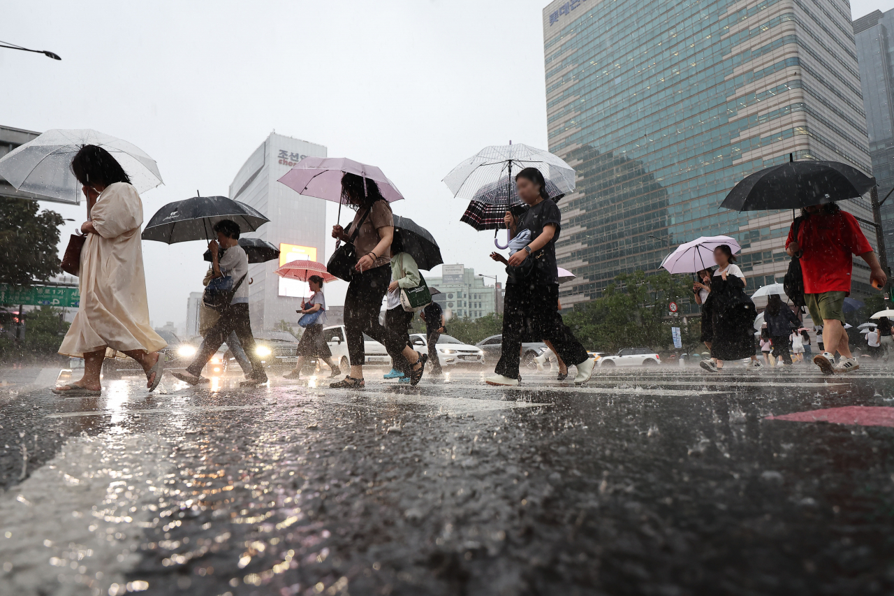 Pedestrians cross the street near Gwanghwamun Square, as a heavy rain warning was issued across the city Wednesday morning. (Yonhap)