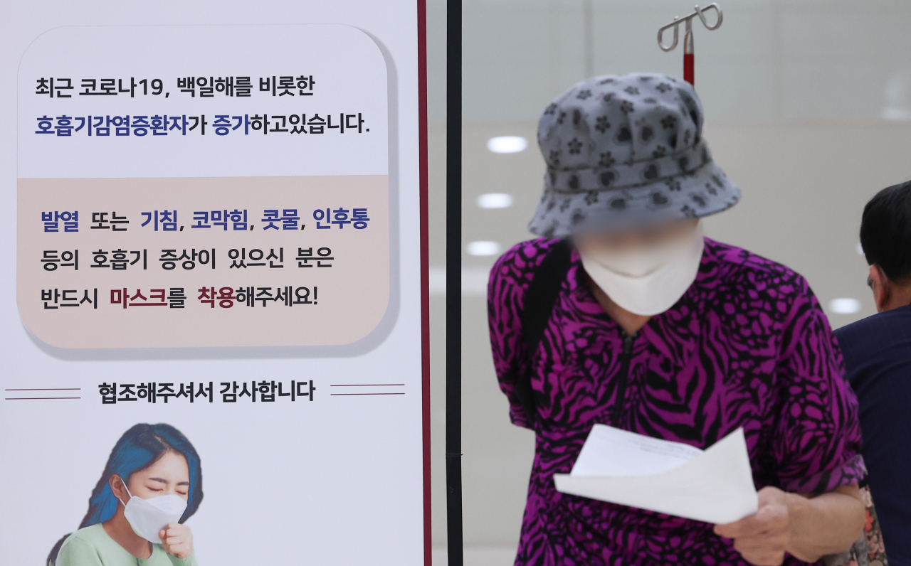 A patient at Korea University Guro Hospital in Seoul,<strong></strong> on Thursday, walks past a poster, recommending visitors to wear face masks in light of the recent resurgence of COVID-19 patients this summer. (Yonhap)