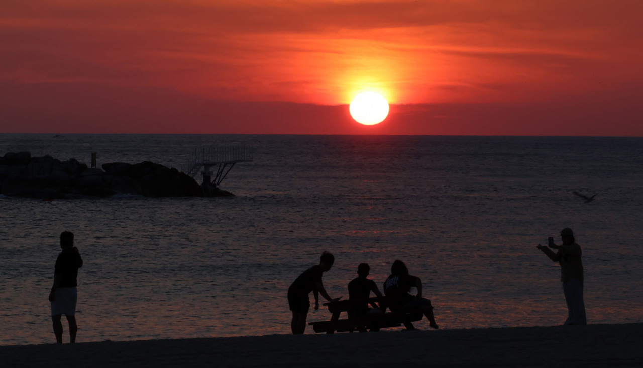 People watch the sunrise on the white sand of Gyeongpo Beach in Gangneung, Gangwon Province, South Korea on Friday. The Korea Meteorological Administration forecast the day's high temperature in Gangneung to reach 36 degrees. (Yonhap)