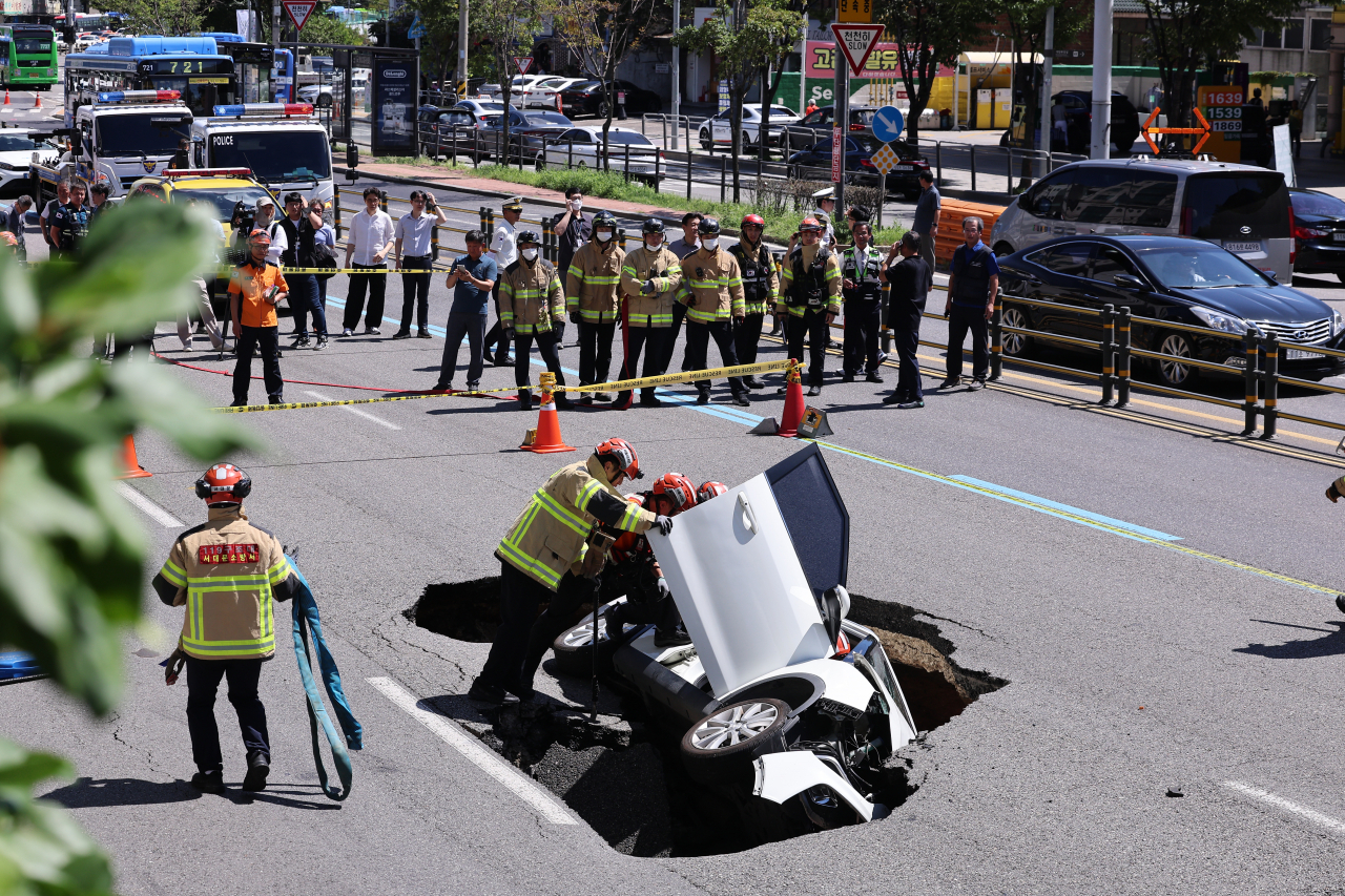 Rescue workers try to rescue passengers from a car swallowed up by a sinkhole that opened up in the middle of Seongsan-ro in Yeonhui-dong, Seodaemun-gu, Seoul on Thursday. (Yonhap)