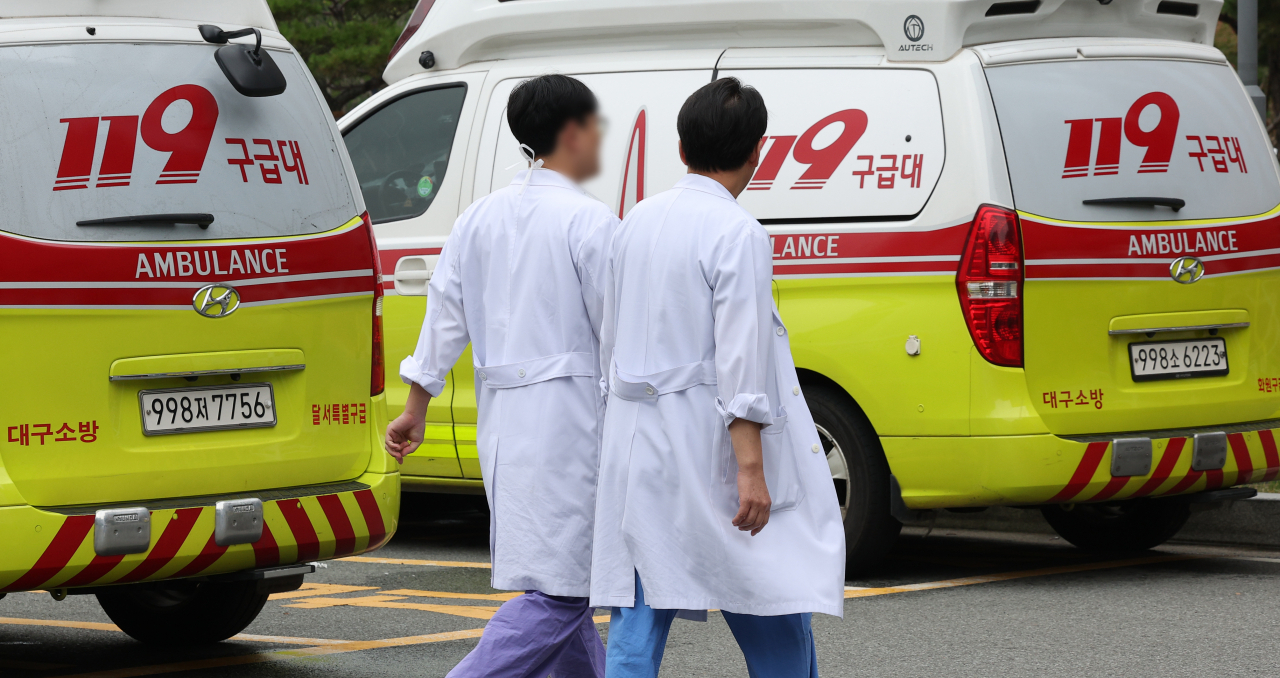 Two medical staff walk in front of ambulances at a hospital in Daegu, Friday. (Yonhap)