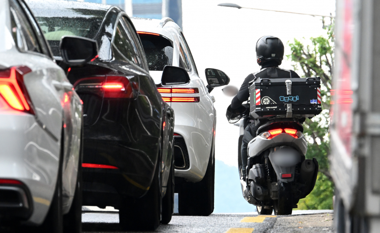 A delivery worker on a motorcycle passes by a line of vehicles in Gangnam-gu, southern Seoul, on July 26. (Im Se-jun/The Korea Herald)