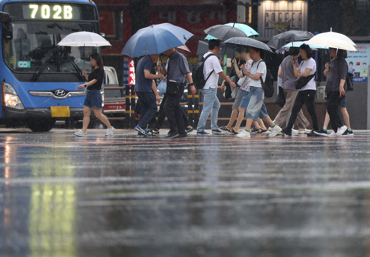 Pedestrians cross the street with umbrellas through the rain on Friday in Jung-gu, central Seoul as the city saw up to 16 millimeters of rain as of 4 p.m. (Yonhap)