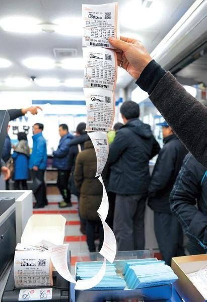 A Seoul lottery shop clerk holds up Lotto tickets. (The Korea Herald)