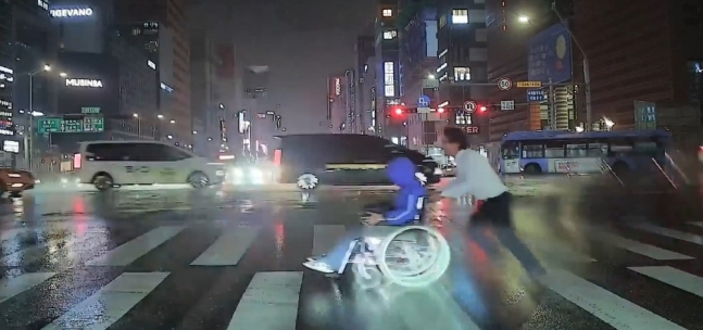 This screengrab from a video provided by the Seoul Bus Labor Union shows bus driver Lee Jung-ho pushing the wheelchair of a man stranded in the middle of a crosswalk in Seoul on Sept.13. (Seoul Bus Labor Union)