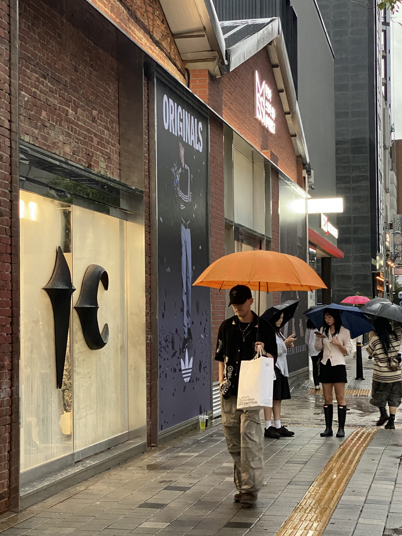 Visitors to Seongsu street walk with umbrellas past the front of Musinsa Store Seongsu @DaerimChanggo on Sept. 20.(Hwang Joo-young/The Korea Herald)