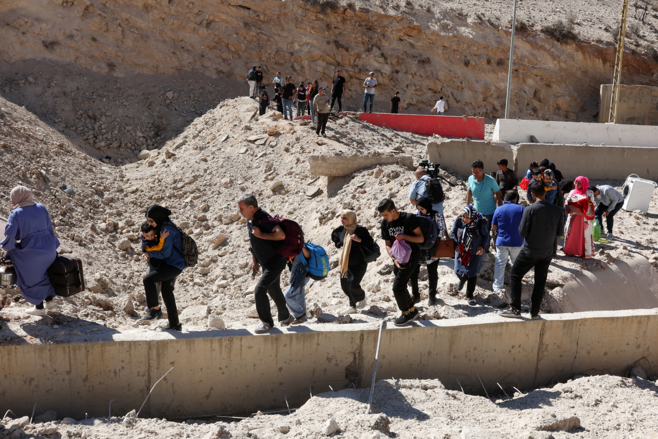 People carry their belongings while walking on the rubble, after an Israeli strike, as they flee Lebanon due to ongoing hostilities between Hezbollah and Israeli forces, at Masnaa border crossing with Syria, in Lebanon, Friday. (Reuters-Yonhap)