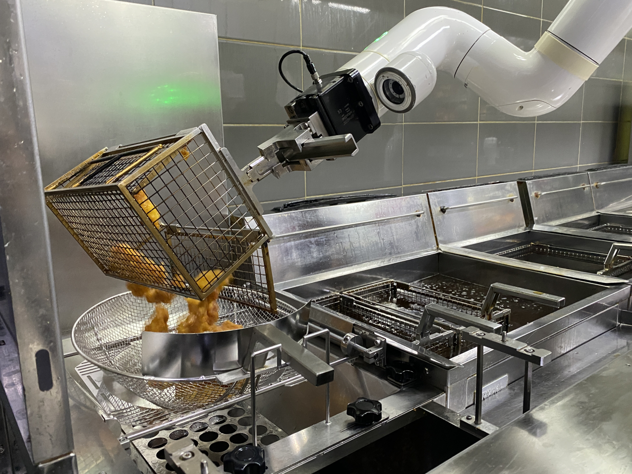 A robot arm transfers fried chicken to a mesh strainer at a Kyochon branch in Namyangju, Gyeonggi Province, Wednesday. (Hwang Joo-young/The Korea Herald)