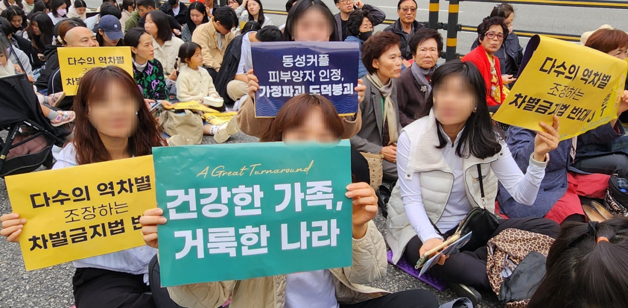 Churchgoers who asked their faces be blurred hold signs at the rally against LGBTQ+ at Seoul Plaza on Sunday. (Choi Si-young/The Korea Herald)