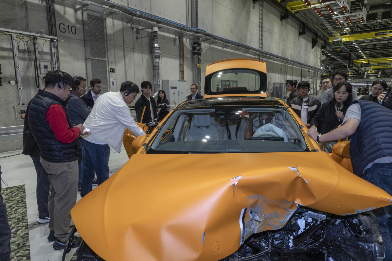 Reporters examine the crumpled front end of the Mercedes EQS 450 electric sedan after the crash test. (Mercedes-Benz)