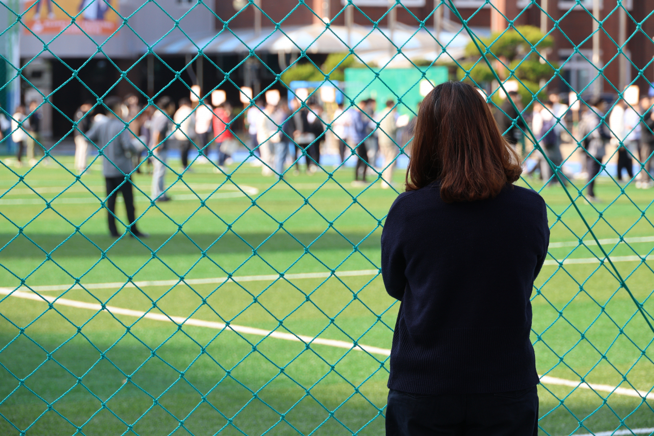 A mother watches her son from a distance as he attends a preliminary CSAT convocation at Chungnam High School in Seo-gu, Daejeon, South Korea, on Nov. 13, a day before the 2025 college entrance exam. (Yonhap)