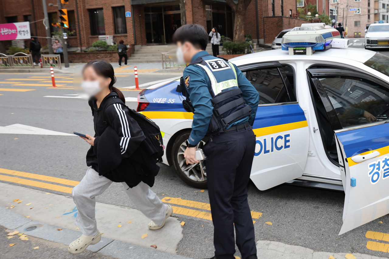 A college aspirant is escorted by police to a test site for the national college entrance exam, in Seoul, Thursday. (Yonhap)