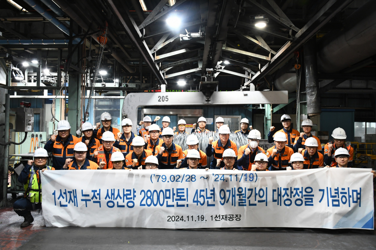 Posco employees at the Unit 1 wire rod mill pose with a banner marking the facility’s cumulative production of 28 million tons over 45 years, in Pohang, North Gyeongsang Province, Tuesday. (Posco Group)