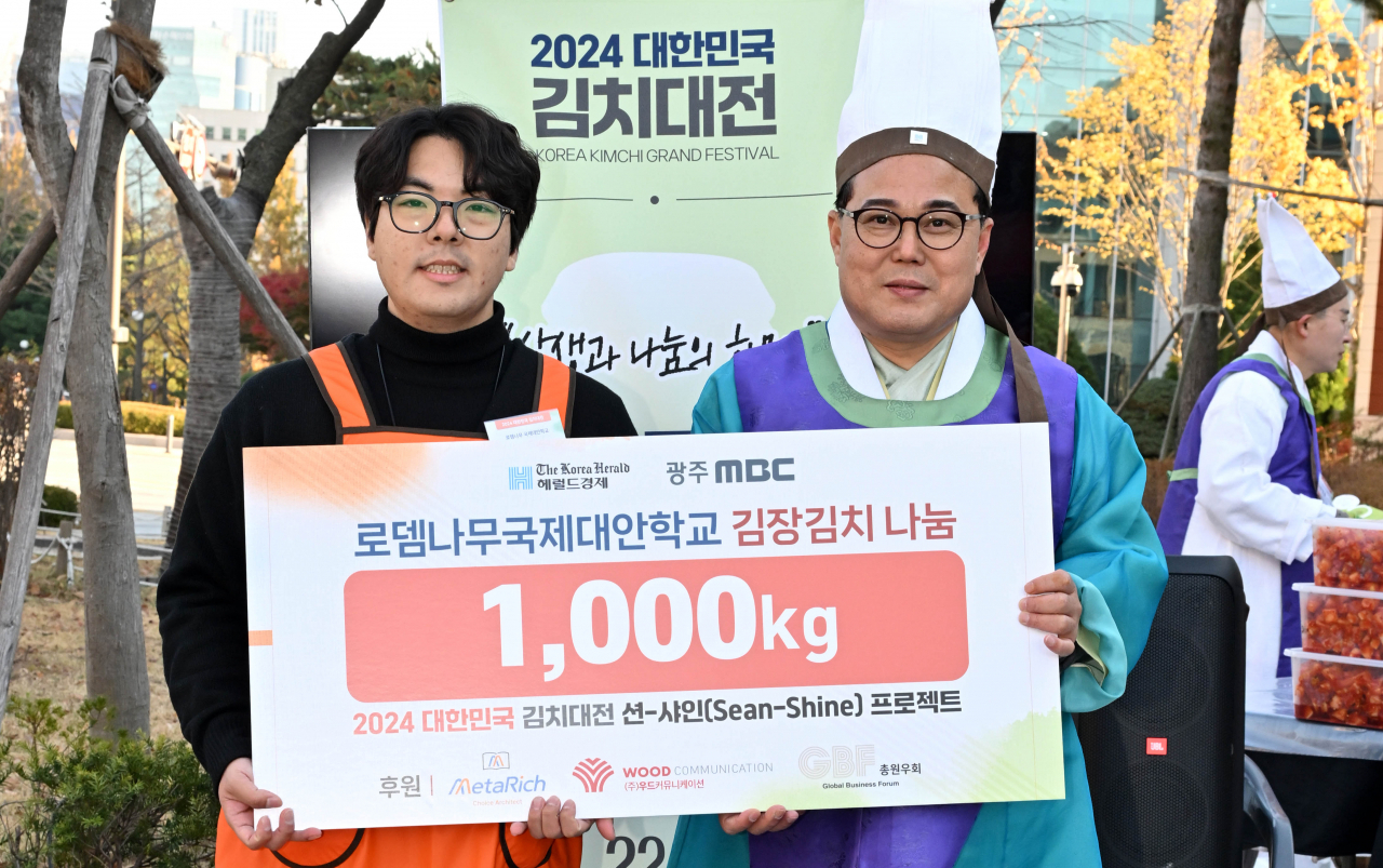 The Korea Herald CEO Kim Young-sang (right, front) gives a panel signifying the donation of a ton of kimchi to a Rodem International Alternative School official on Monday. (Im Se-jun/The Korea Herald)