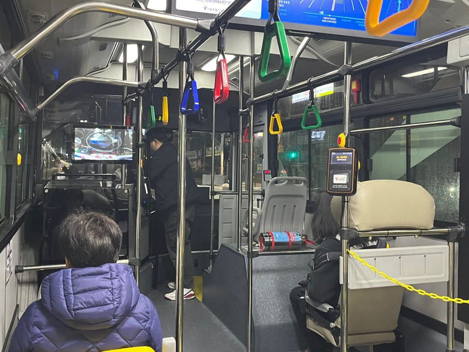 On the A160 bus early Friday morning in Seoul, a safety officer in the driver's seat and a service manager converse during the vehicle's autonomous operation, while passengers watch the steering wheel move automatically on the monitor. (The Korea Herald / Lee Jaeeun)