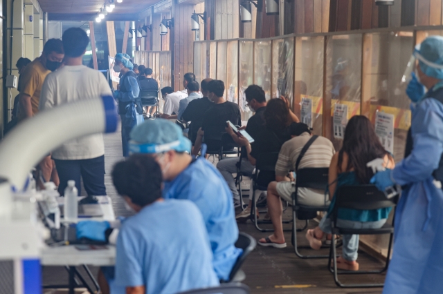 People sit in line to receive tests at a COVID-19 testing center in Seoul on Tuesday. (Yonhap)