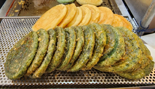 Hotteok -- original with glutinous rice (top) and with mugwort batter -- are displayed at a street vendor at Gwangjang Market in Jongno, central Seoul, Tuesday. (Hwang Dong-hee/The Korea Herald)