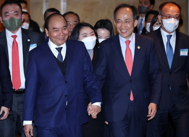 Vietnamese President Nguyen Xuan Phuc (left) and South Korean Finance Minister Choo Kyung-ho hold hands while attending the Korea-Vietnam Business Forum held at Lotte Hotel Seoul, Tuesday. (KCCI)