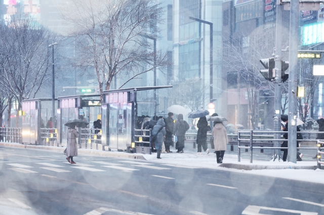 Morning commuters wait for buses on Wednesday morning, when a heavy snow advisory was issued across Seoul. The advisory was lifted in the morning, but snow is expected to continue until Saturday. (Yonhap)