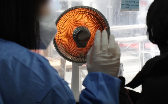 A heatlh worker warms herself up in front of an electric heater at a testing center in Mapo Ward in Seoul on Monday. (Yonhap)