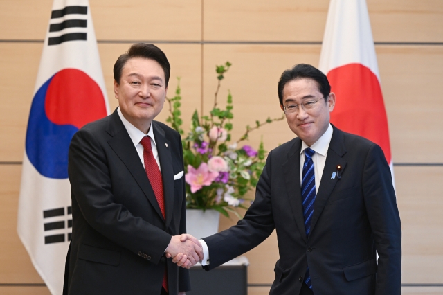 South Korean President Yoon Suk Yeol and Japanese Prime Minister Fumio Kishida shake hands ahead of summit talks in Tokyo on March 16. (Yonhap)