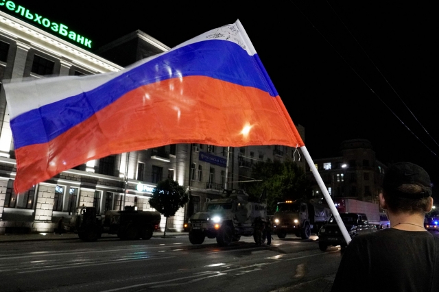 A man waves the Russian national flag as the members of Wagner group prepare to pull out from the headquarters of the Southern Military District to return to their base in Rostov-on-Don late on Saturday. Rebel mercenary leader Yevgeny Prigozhin who sent his fighters to topple the military leaders in Moscow will leave for Belarus and a criminal case against him will be dropped as part of a deal to avoid 