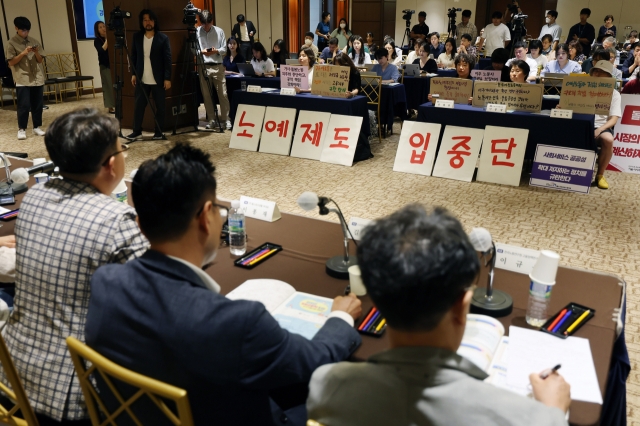 Civic groups protest a pilot project to introduce 100 foreign domestic workers in the middle of a public hearing, holding signs that read 