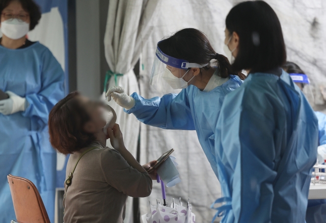 Quarantine officials in blue gowns conduct a PCR test at a screening center in Dalseo-gu, Daegu, Wednesday. (Yonhap)