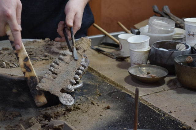 Lim brushes off sand to inspect the final product, after the molten metal has solidified. (Kim Hae-yeon/ The Korea Herald)