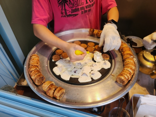 Lee Jeong-soo, a kukhwappang vendor, flips the snacks in the cast iron frame. (Lee Jung-youn/The Korea Herald)