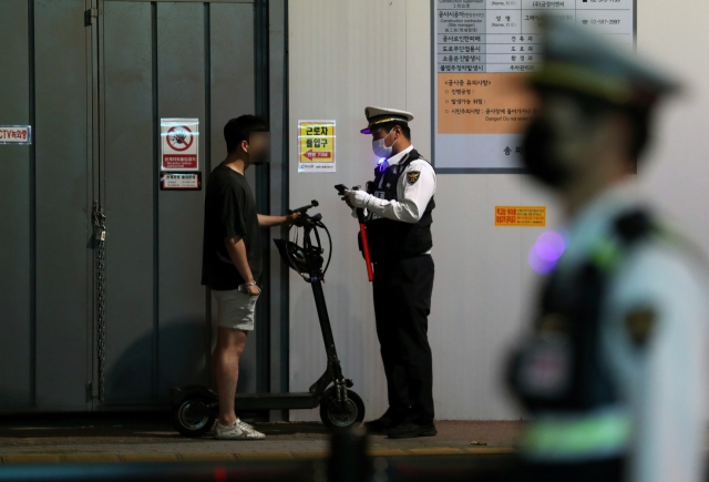 A police officer tells an e-scooter rider to wear a helmet in Seoul's Songpa-gu, May 30, 2022. (Newsis)