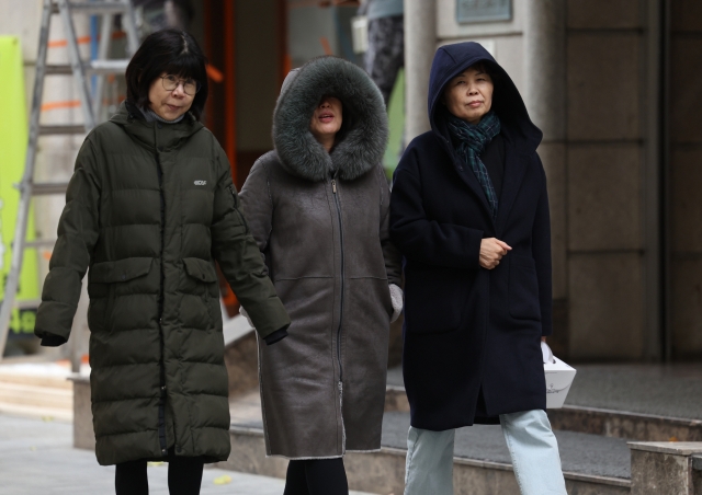 People walk in heavy winter clothes in Seoul on Friday as morning temperatures drop to below 0 degrees Celcius. (Yonhap)