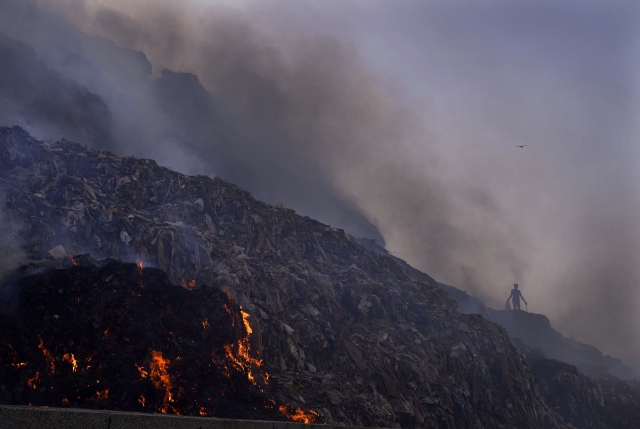 A person picks through trash for reusable items as a fire rages at the Bhalswa landfill in New Delhi, April 27, 2022. A new United Nations report estimates that 19% of the food produced around the world went to waste in 2022. (AP)