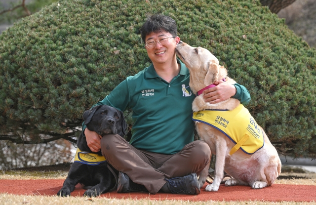 Park Tae-jin sits beside 6-year-old guide dog Haedal (left) and 6-year-old trained dog Genie at Samsung Guide Dog School in Yongin, Gyeonggi Province, March 27. (Im Se-jun/ The Korea Herald)