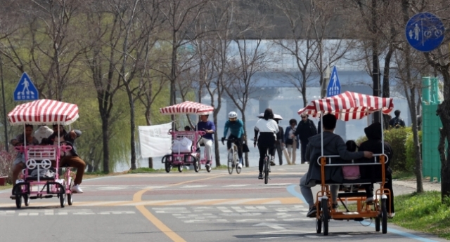 Parkgoers enjoy the day by riding four-wheel bicycles along the Han River, in Yeouido, Seoul. (Yonhap)