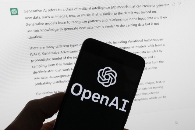 The OpenAI logo is seen on a mobile phone in front of a screen displaying output from ChatGPT in Boston on March 21, 2023. (AP-Yonhap)