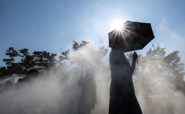 People walk through cooling mist while holding parasols to avoid the heat in Daegu on Tuesday, when a heat wave advisory was issued for the southeastern city. (Yonhap)